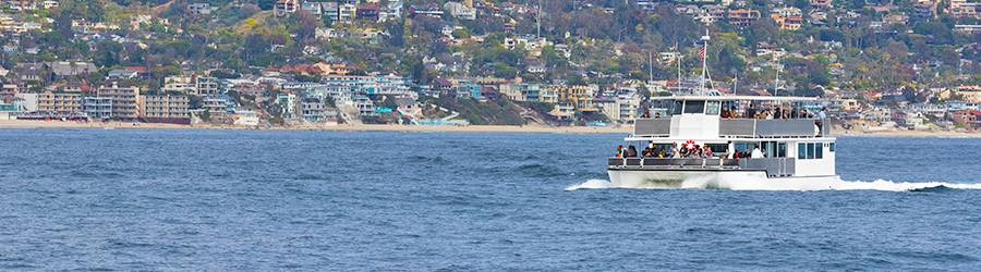 A whale watching boat full of whale watchers travels along the coast of Newport Beach, CA